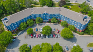 Aerial Exterior of Centennial Court, beautifully groomed grounds, view of parking lot, lush foliage, building painted blue.