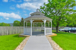 Outdoor Gazebo, stones lining the sidewalk, beautiful tree nearby, picket fence, parking out front.