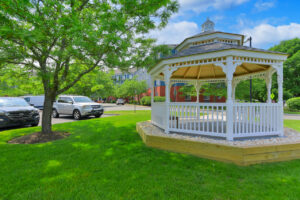 Outdoor Gazebo, stones lining the sidewalk, beautiful tree nearby, picket fence, parking out front.